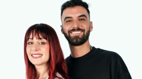 Studio televisivo notturno con fuoco acceso, due persone sedute di fronte in un falò di confronto serale, immagine di approfondimento